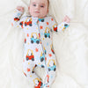 Baby wearing a colorful onesie with vehicle patterns on a white blanket