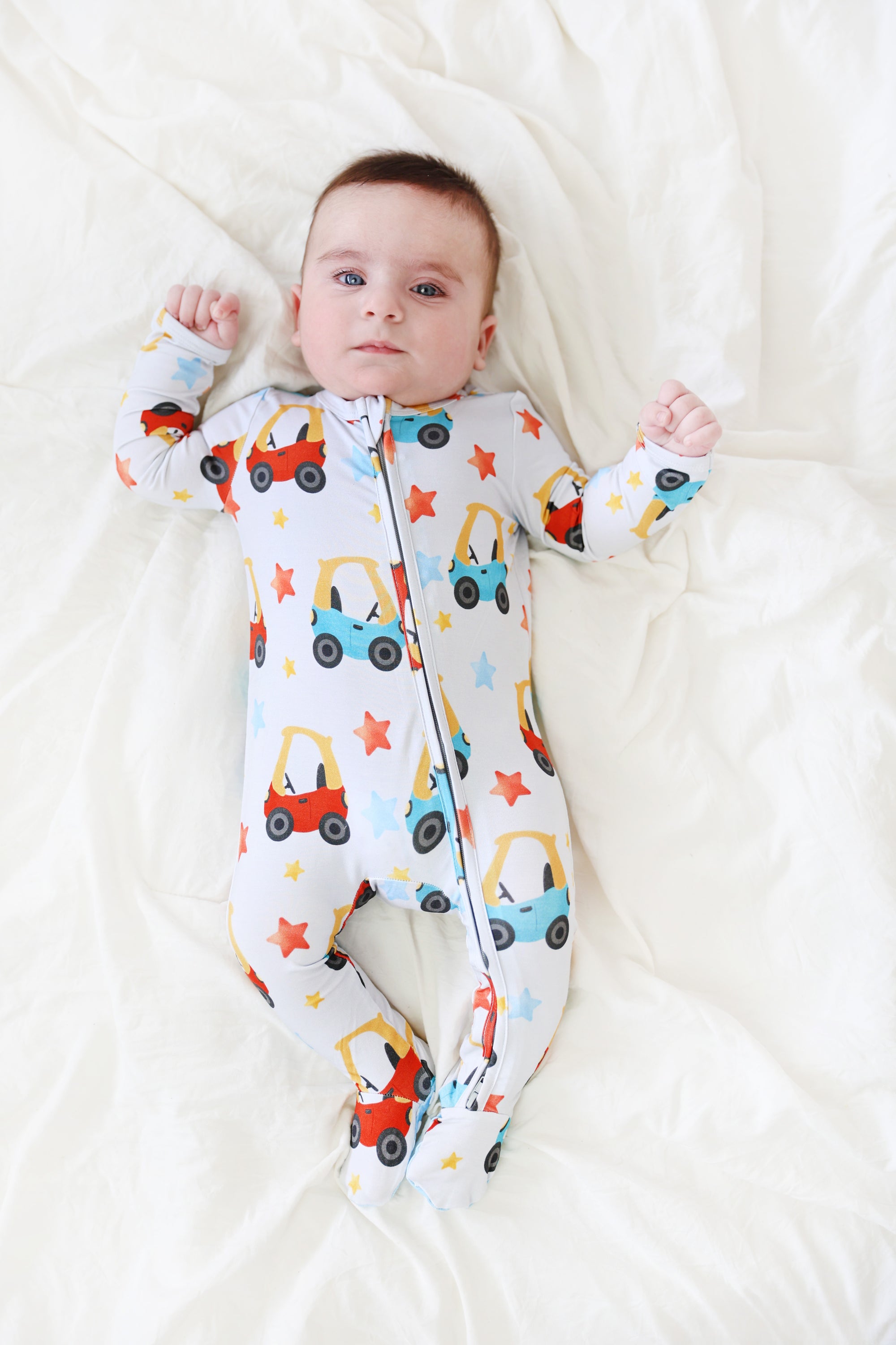 Baby wearing a colorful onesie with vehicle patterns on a white blanket