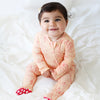 Baby in a pink floral outfit sitting on a white bed