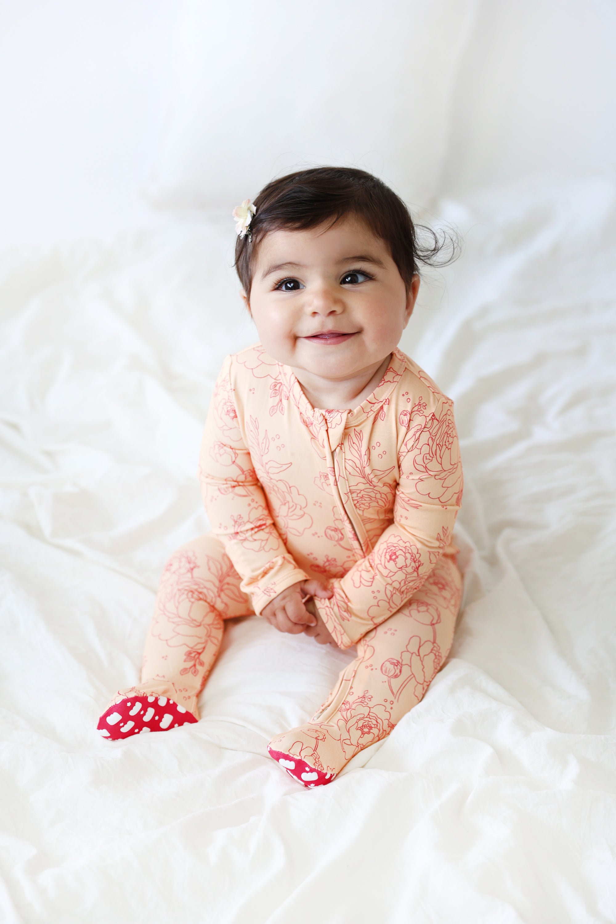 Baby in a pink floral outfit sitting on a white bed