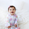 Baby wearing a colorful onesie with butterfly design on a white blanket