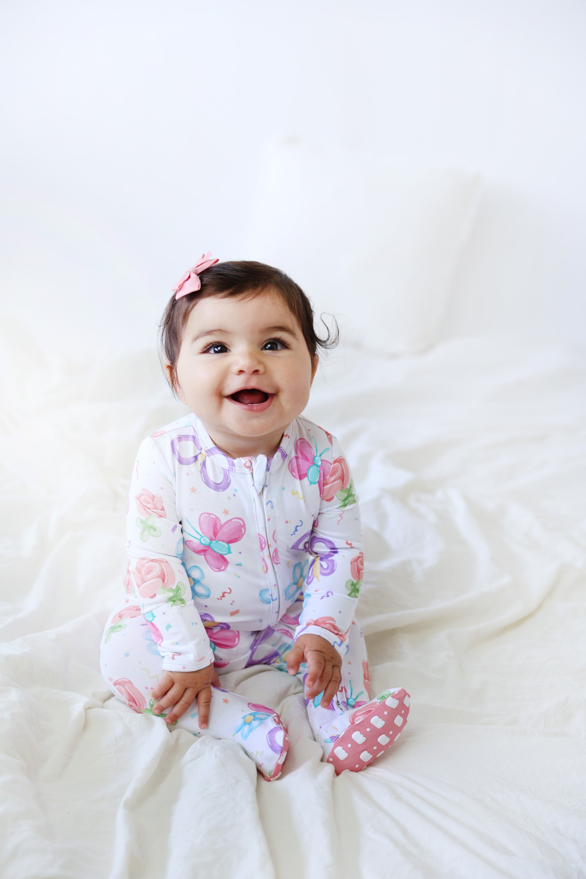 Baby wearing a colorful onesie with butterfly design on a white blanket