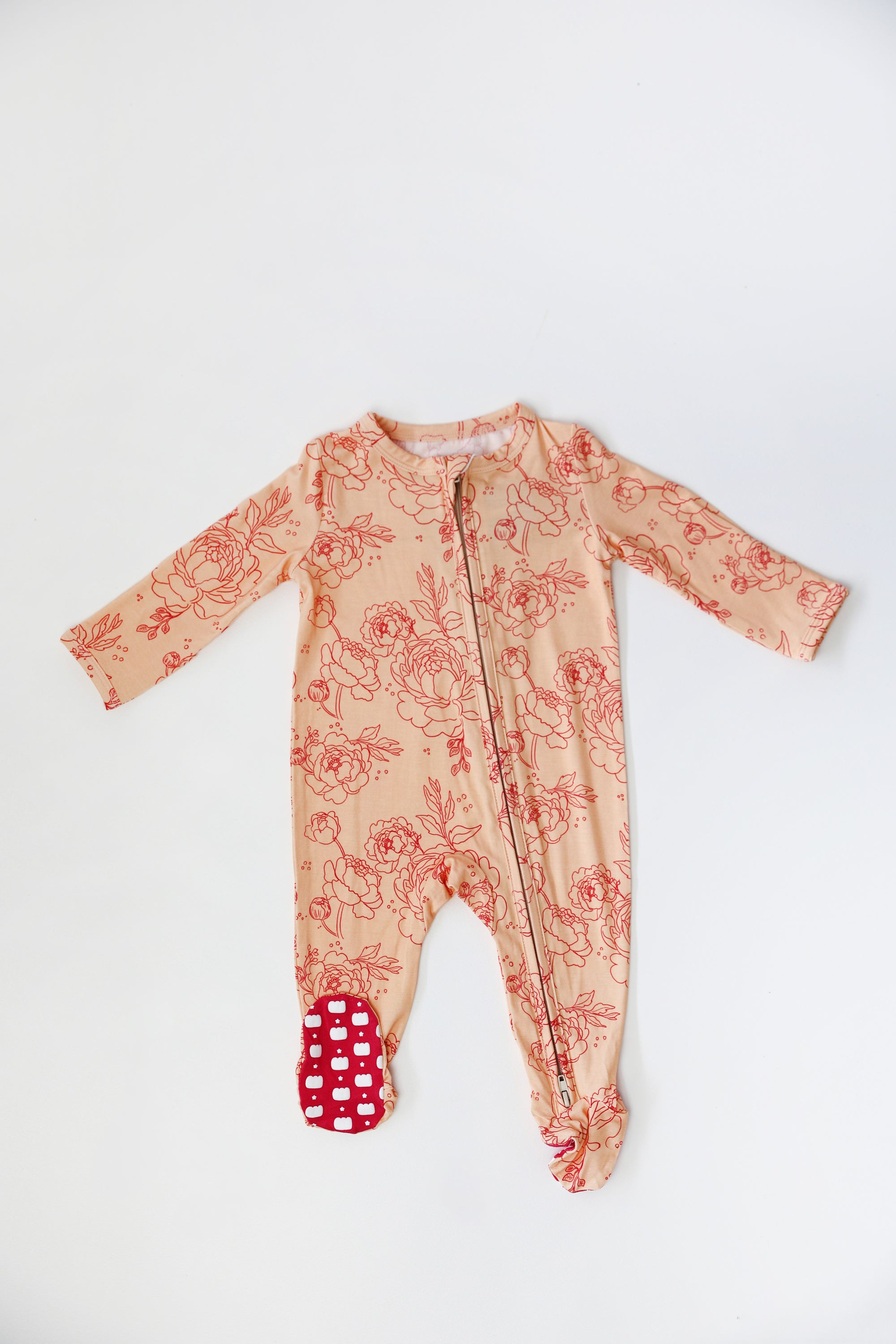 Baby onesie with floral pattern and red polka dot feet on a white background